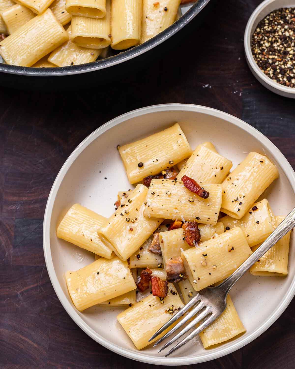 White plate with rigatoni alla gricia on walnut cutting board.