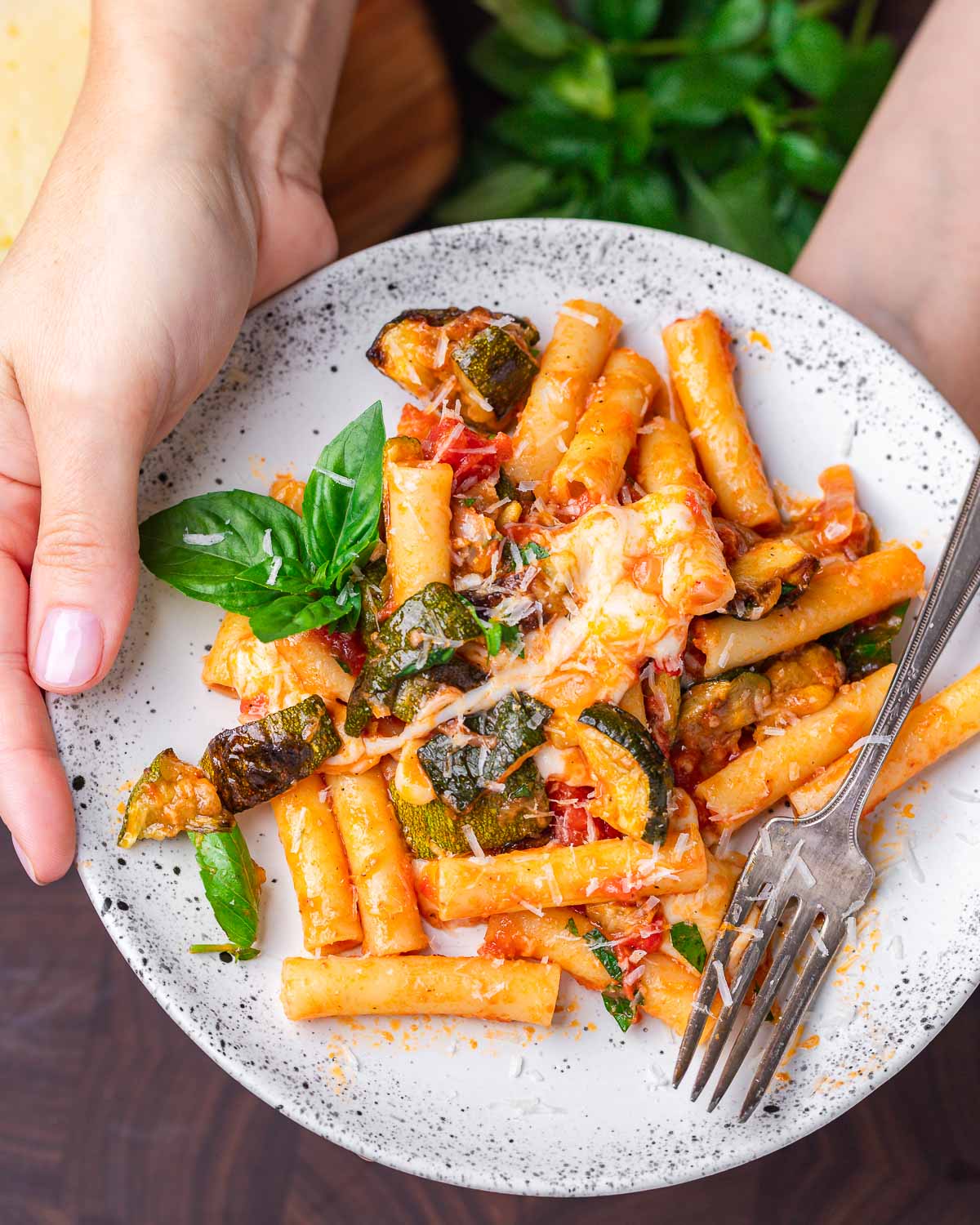 Hands holding white plate with spicy roasted zucchini pasta.