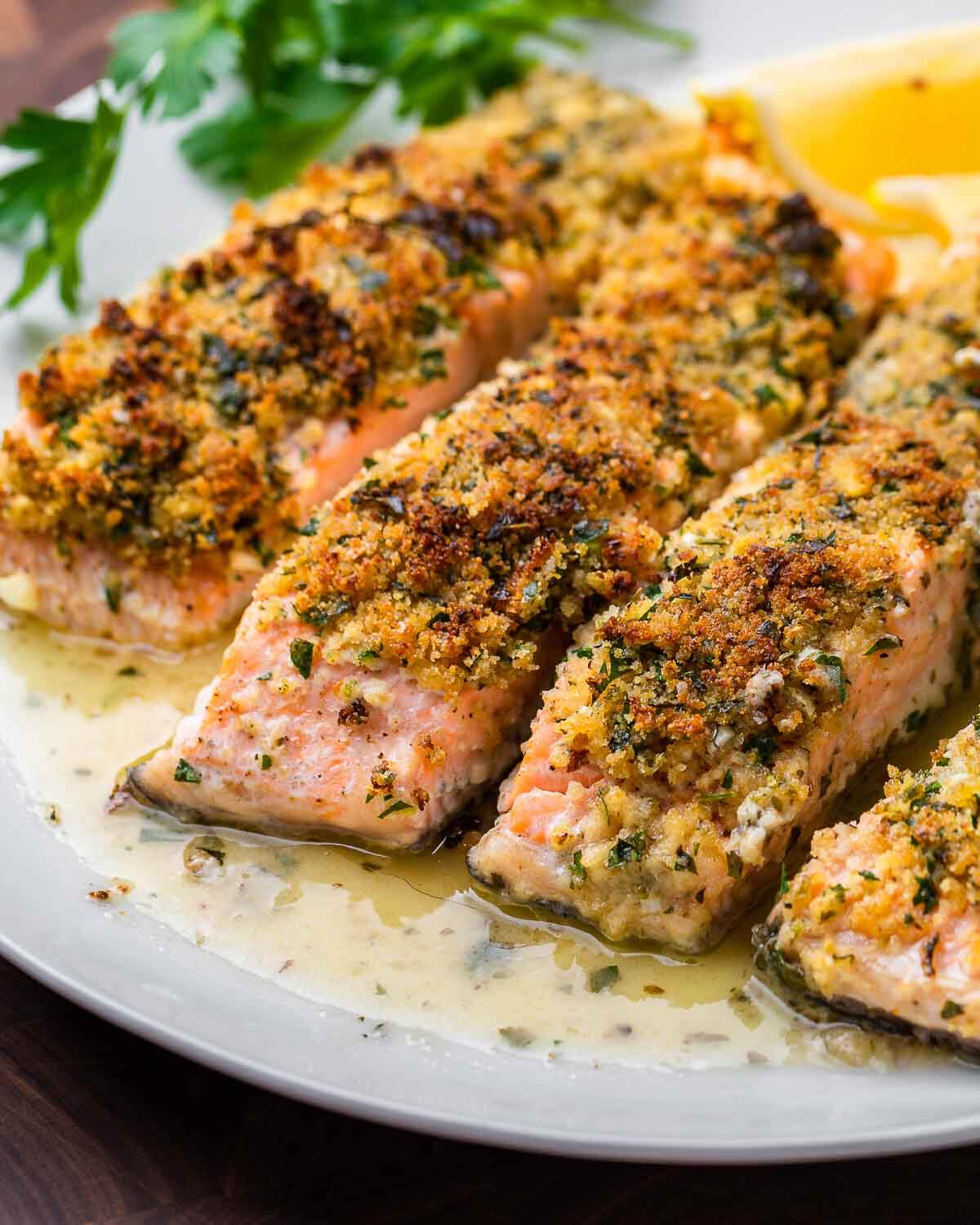 Salmon oreganata in butter sauce on white plate.