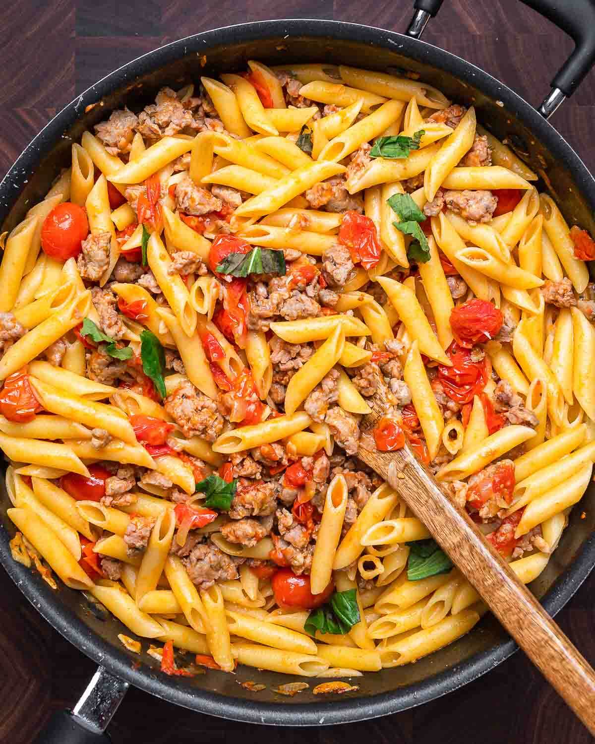 Overhead shot of sausage cherry tomato pasta in black pan.