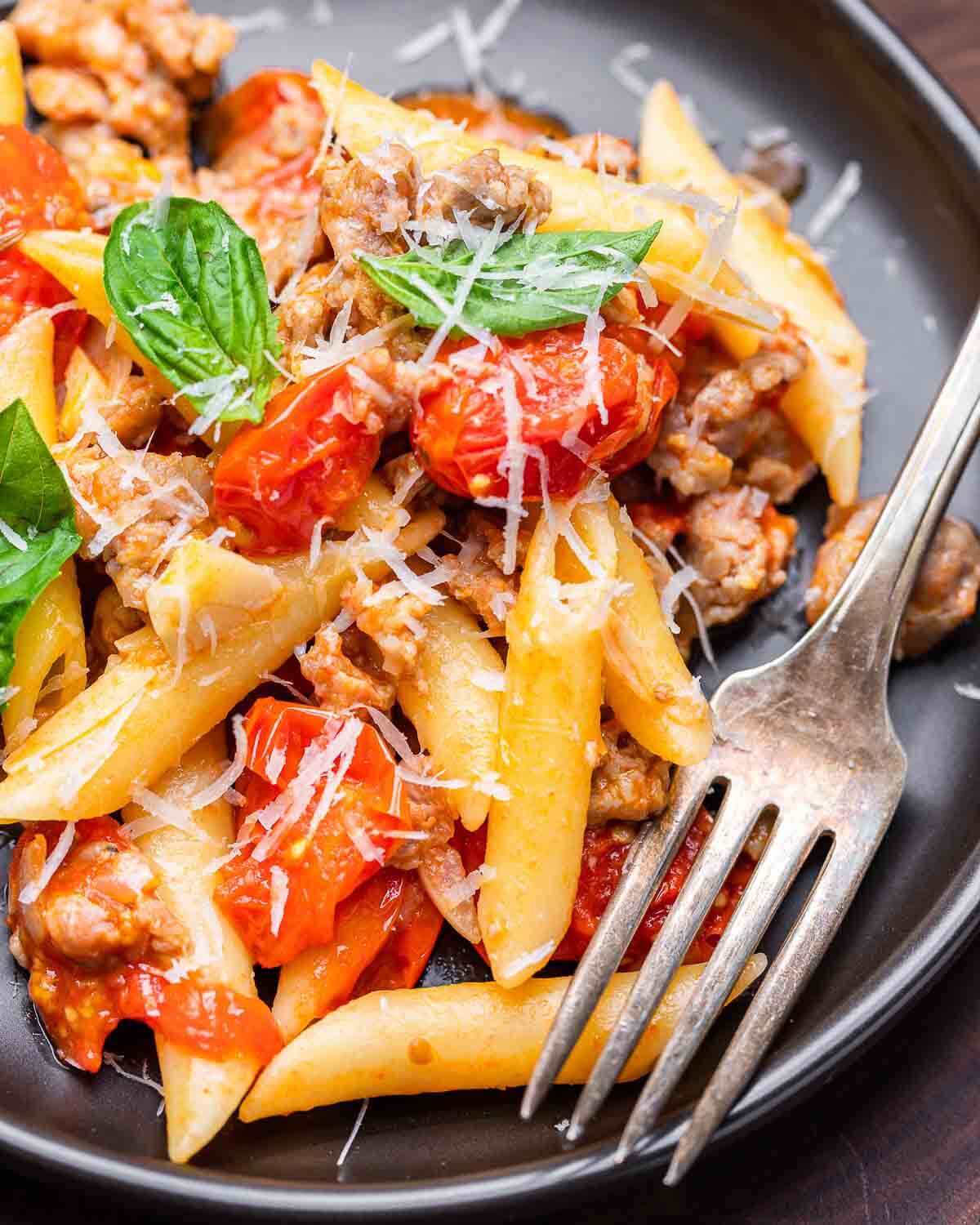 Closeup shot of black plate with sausage cherry tomato pasta.