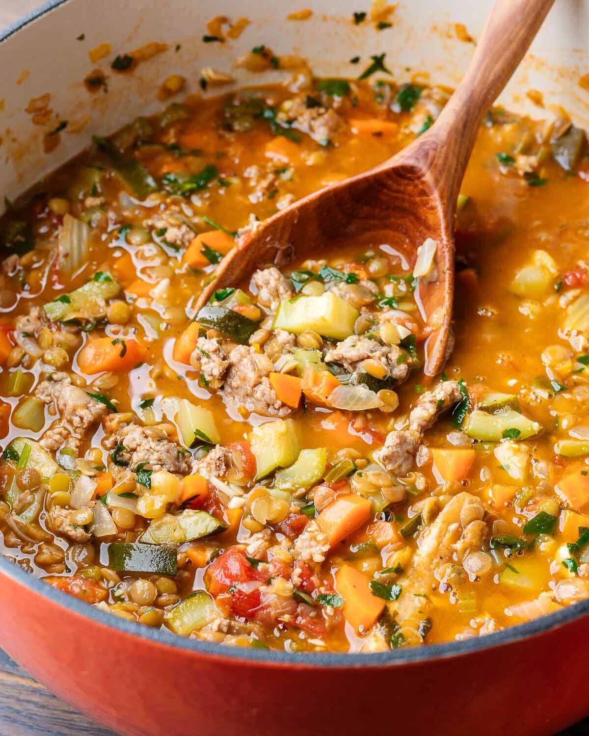 Sausage lentil soup in large Dutch oven with wooden ladle.