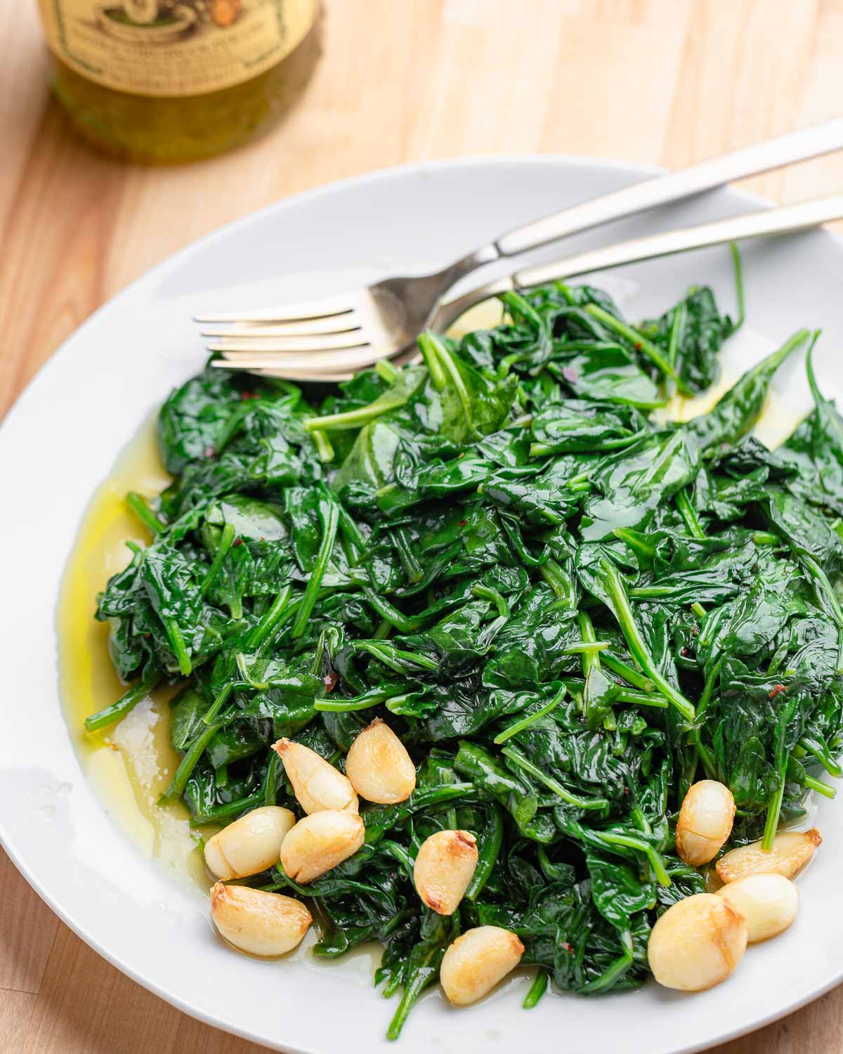 White plate with sauteed garlic spinach and whole garlic cloves.