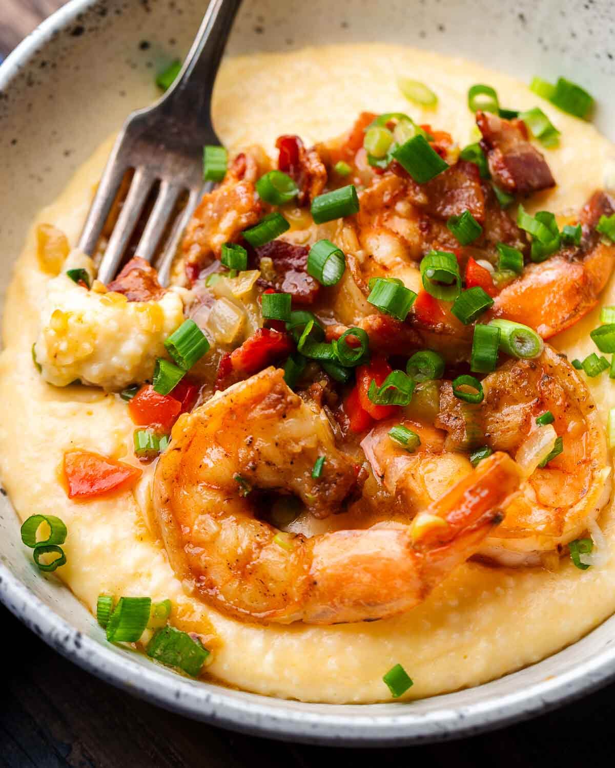 White bowl with shrimp and grits with fork dipped into grits.