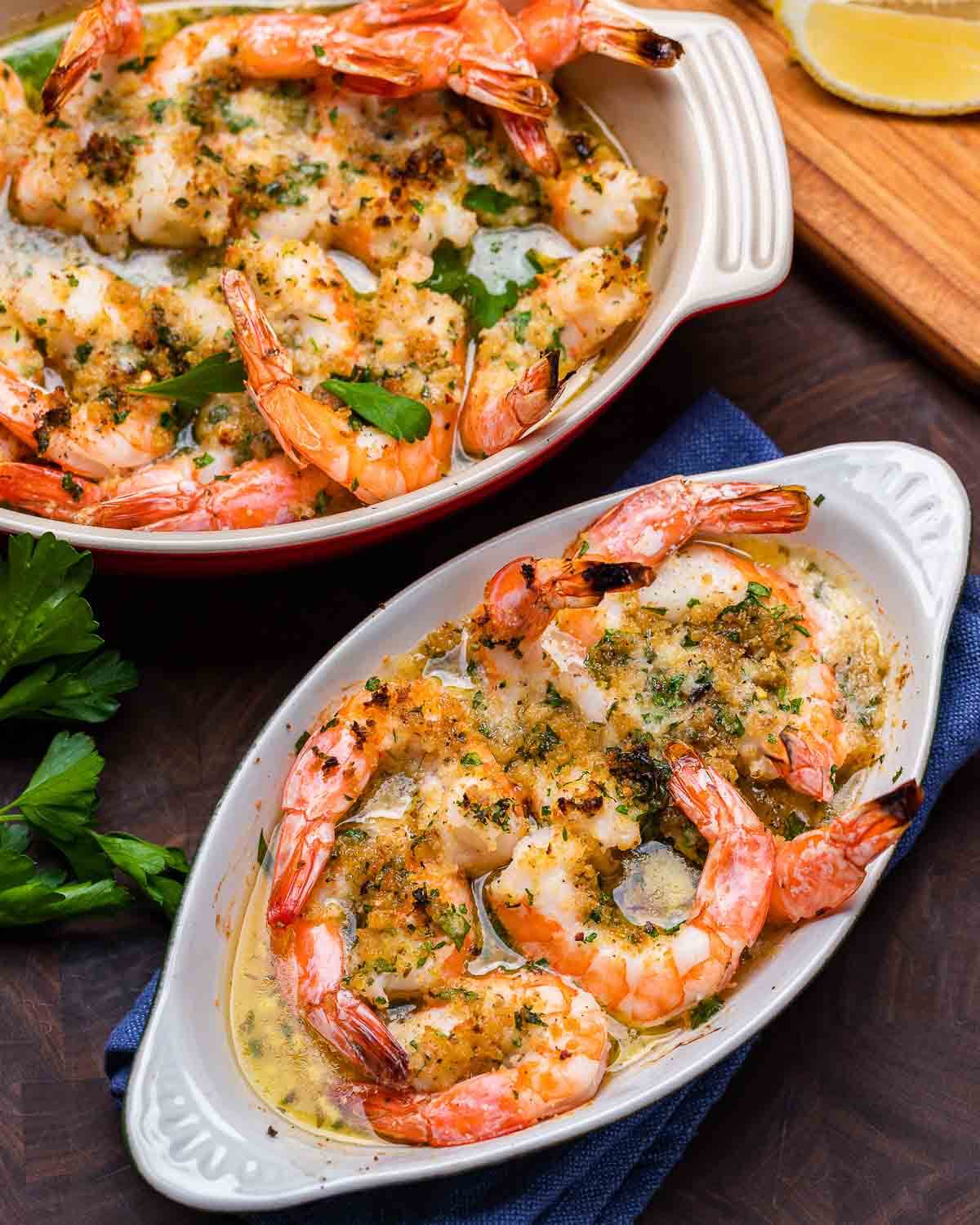 Large and small dish of baked shrimp oreganata on walnut cutting board.