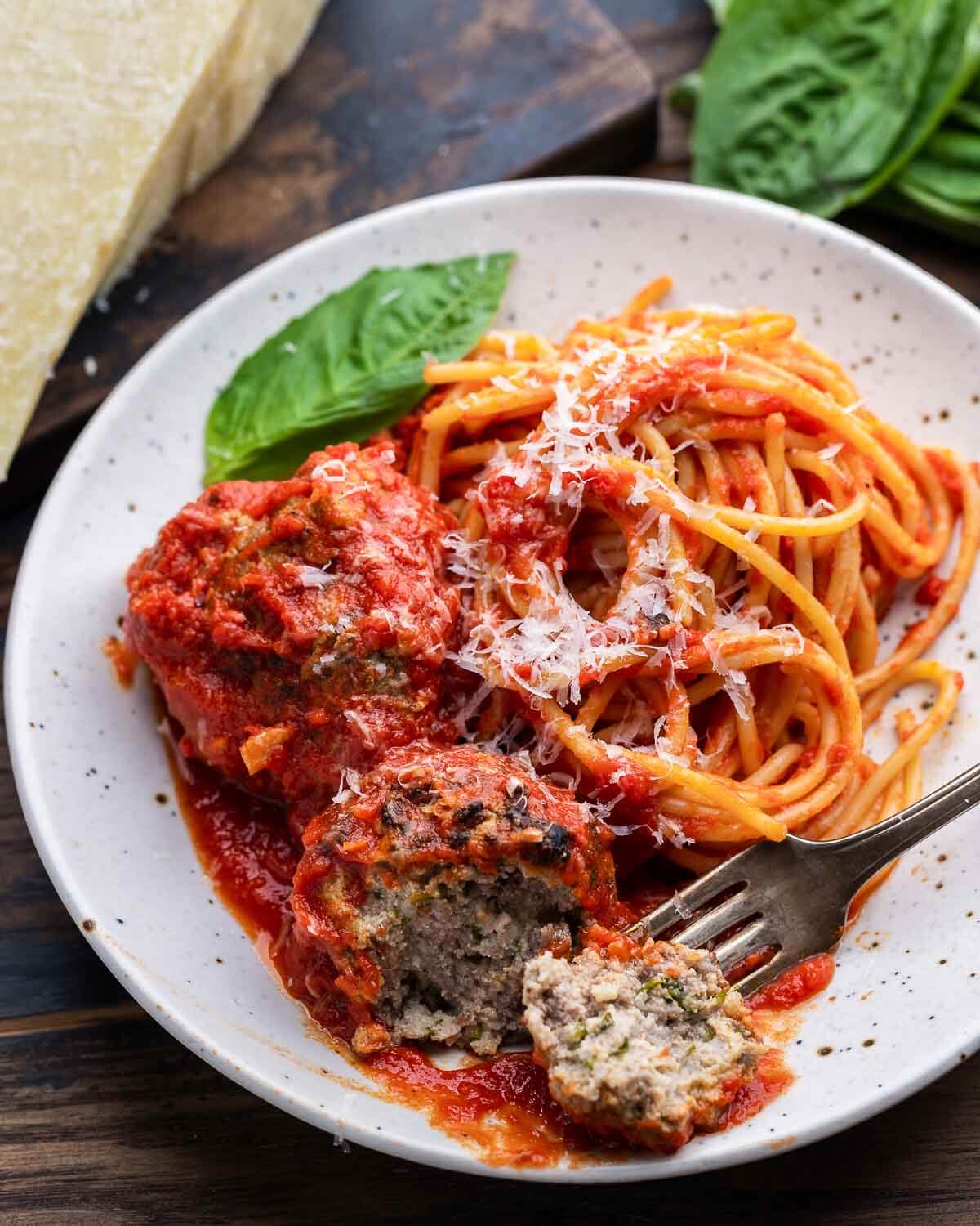 Spaghetti and meatballs in white plate with one meatball cut in half.