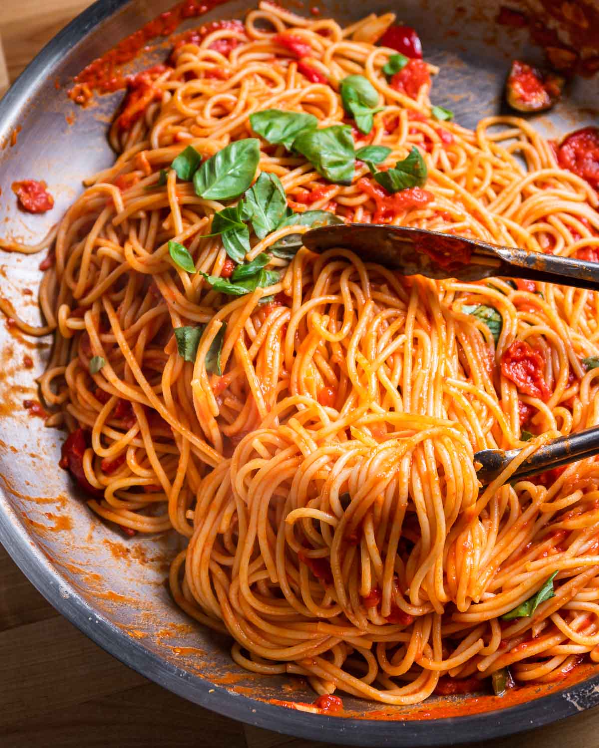 Spaghetti arrabbiata in steel pan with tongs.