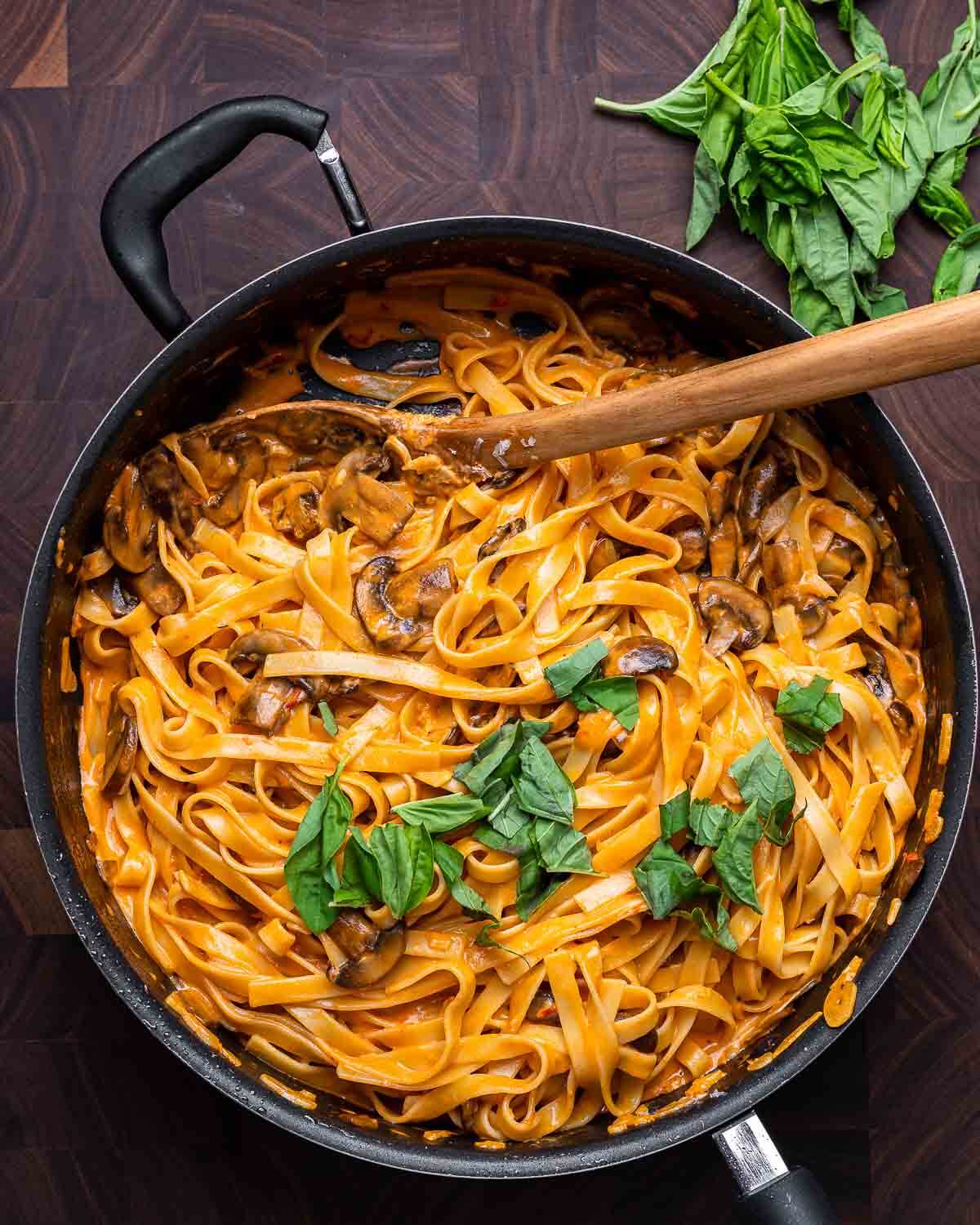 Overhead shot of spicy creamy mushroom pasta in black pan and bunch of basil on the side.