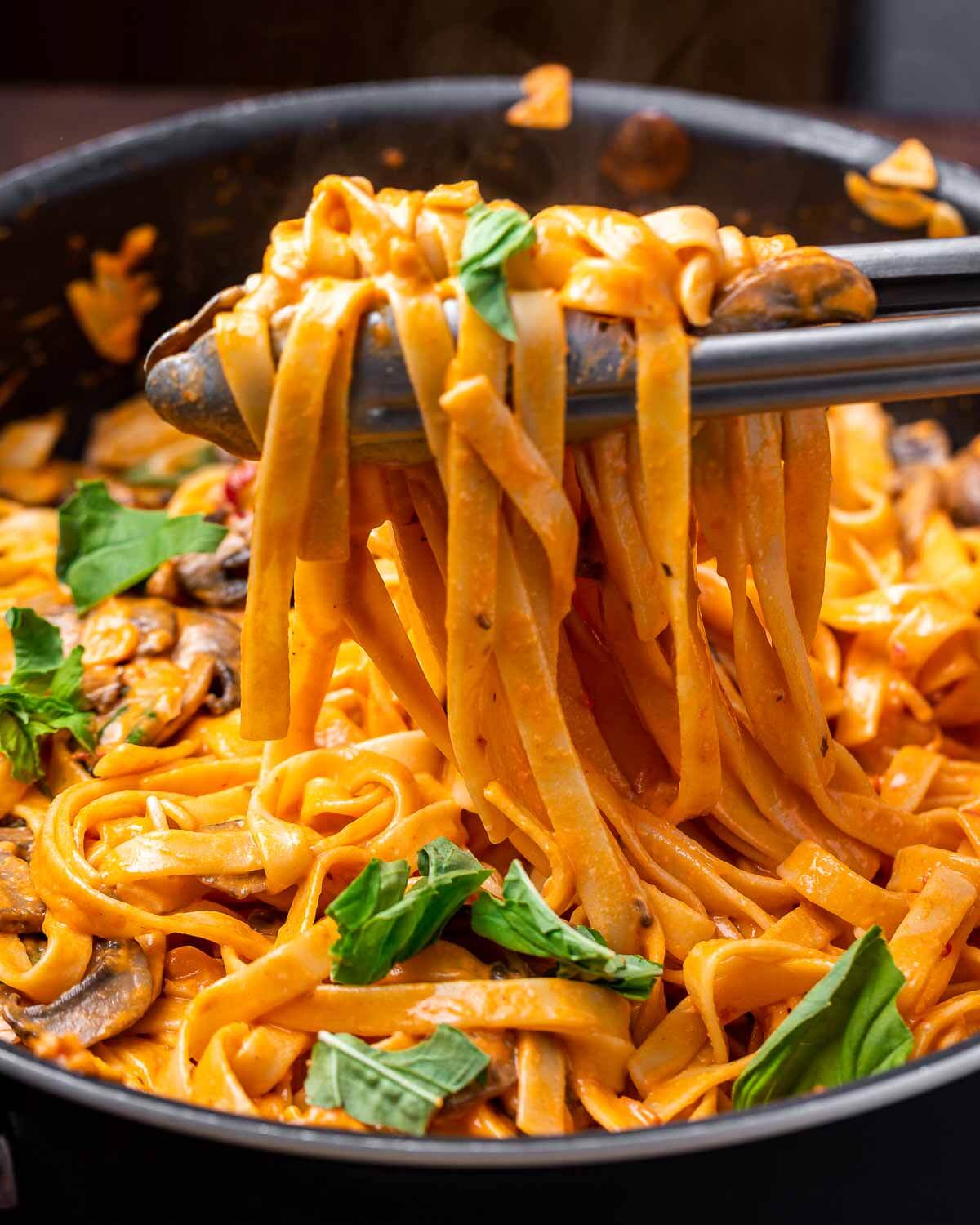 Tongs holding spicy Calabrian fettucine mushroom pasta.