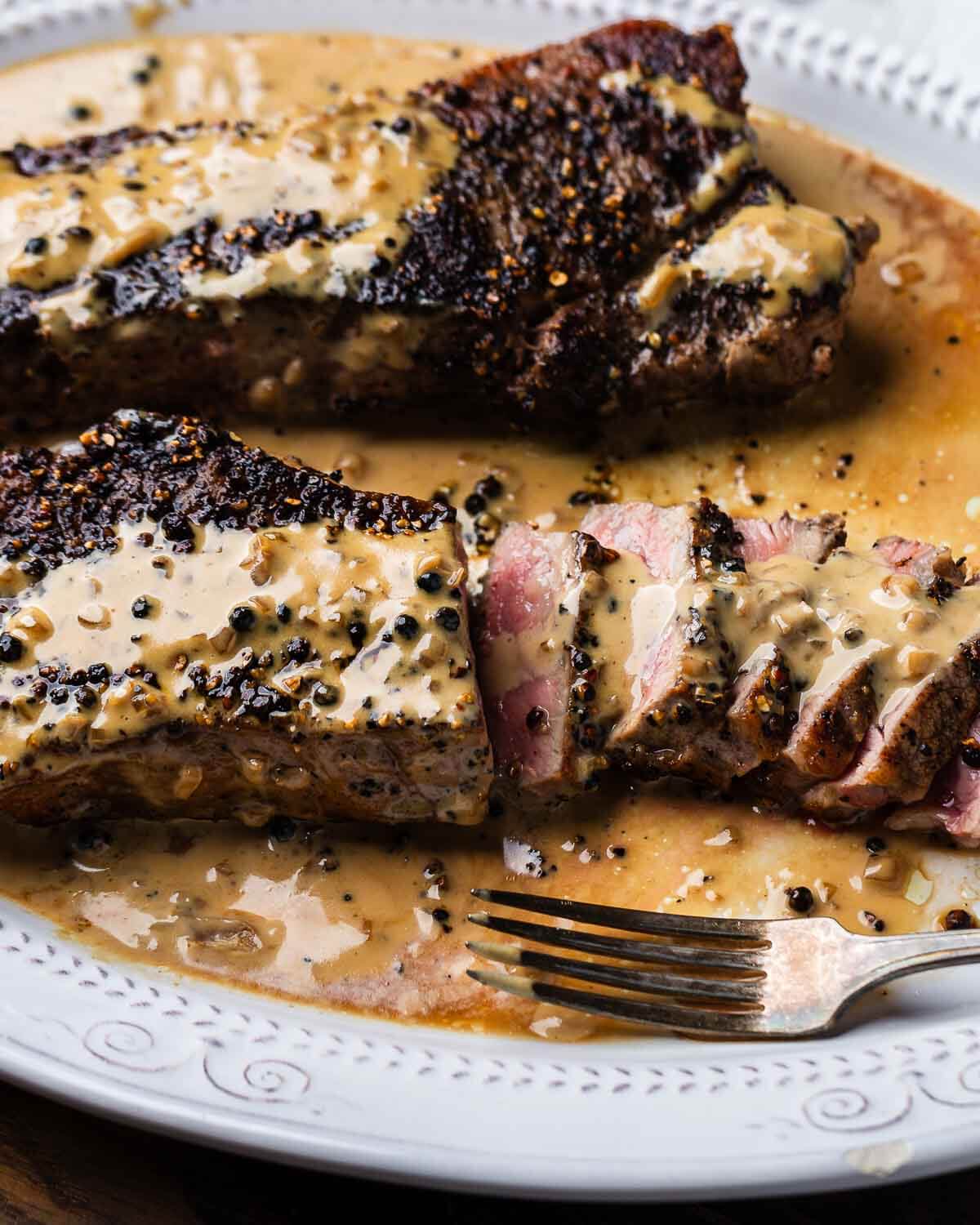 Sliced New York strip steak au poivre in white plate.