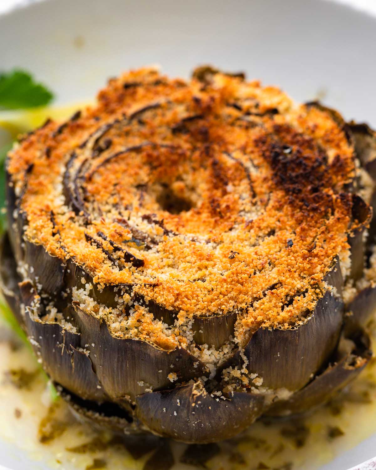 Italian stuffed artichoke on white plate.