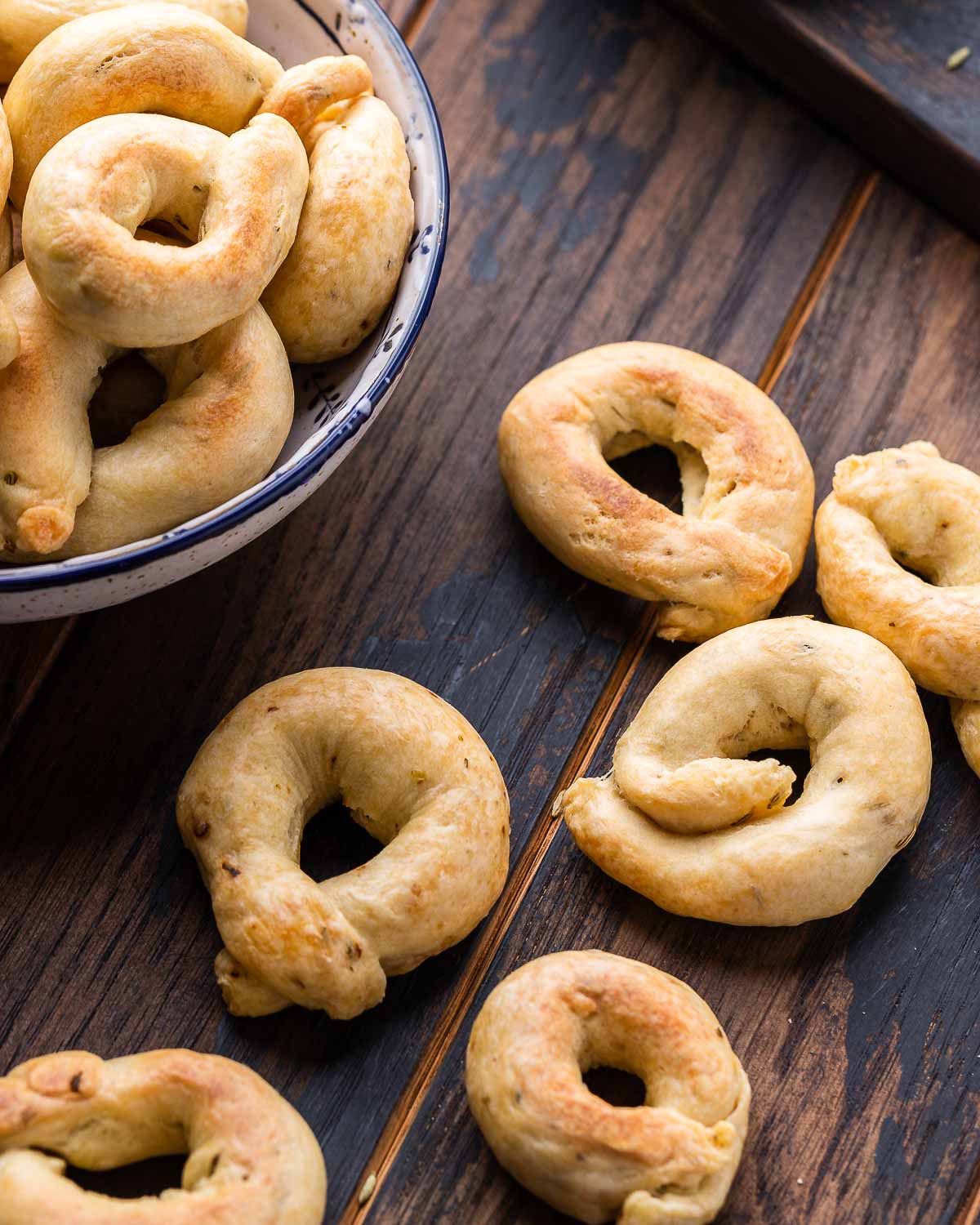 Taralli spread out on a walnut board with bowl in the background.