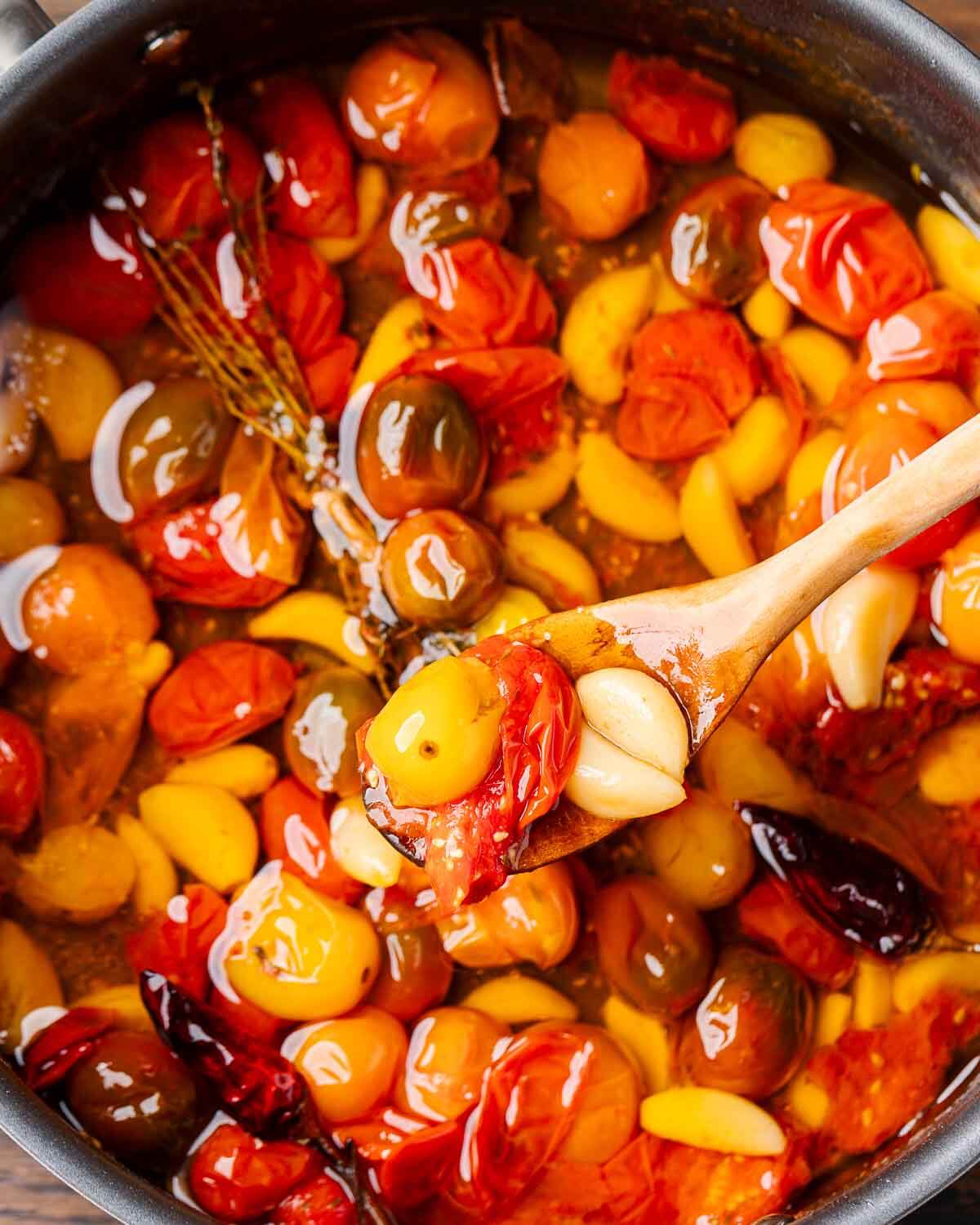 Overhead shot of spoon holding tomato garlic confit over pan.