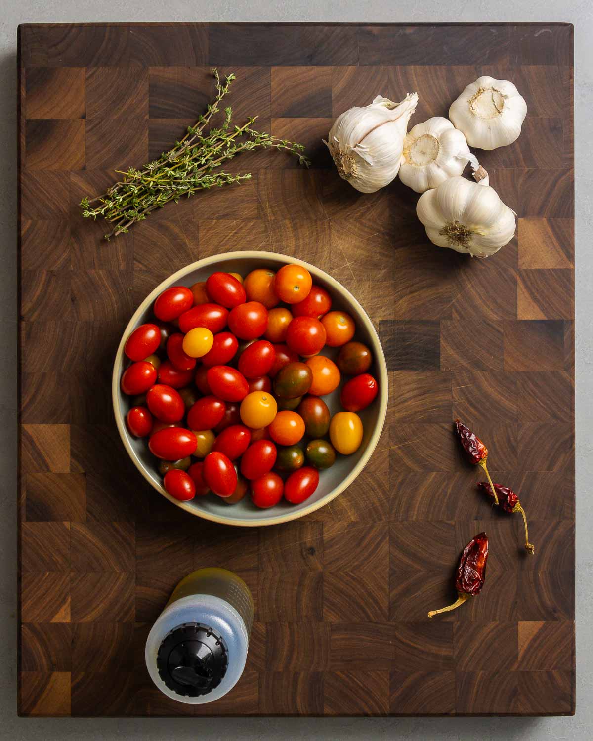 Ingredients shown: thyme, garlic, cherry and grape tomatoes, dried hot chili peppers, and extra virgin olive oil.