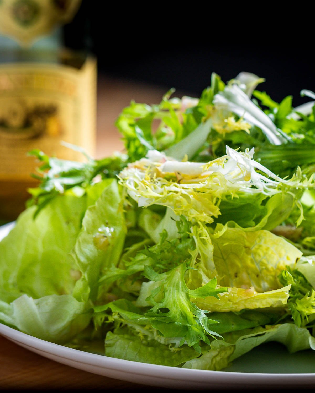 Plate of piled high lettuce greens with bottle of olive oil in background.