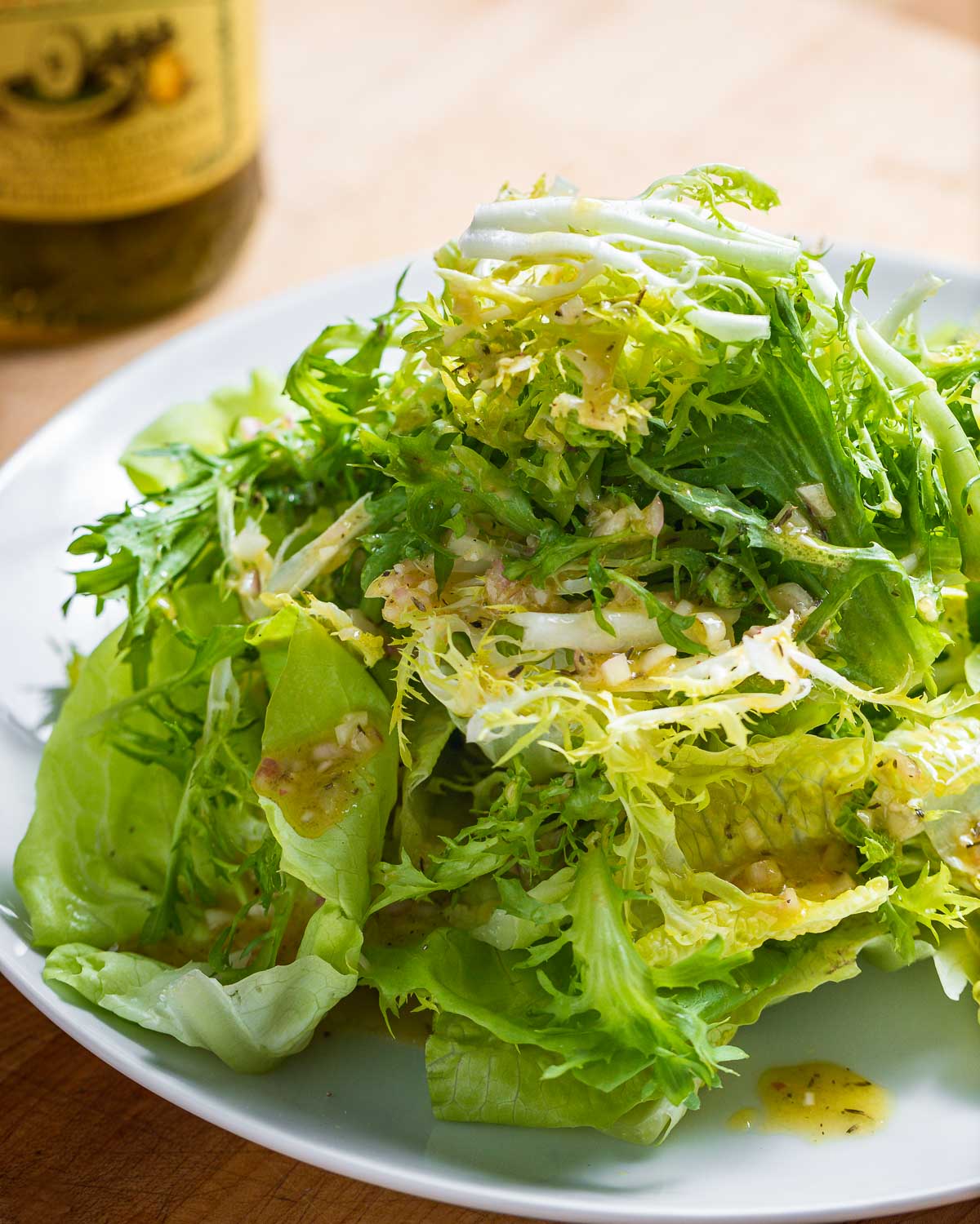 Plate of piled high lettuce greens with vinaigrette.